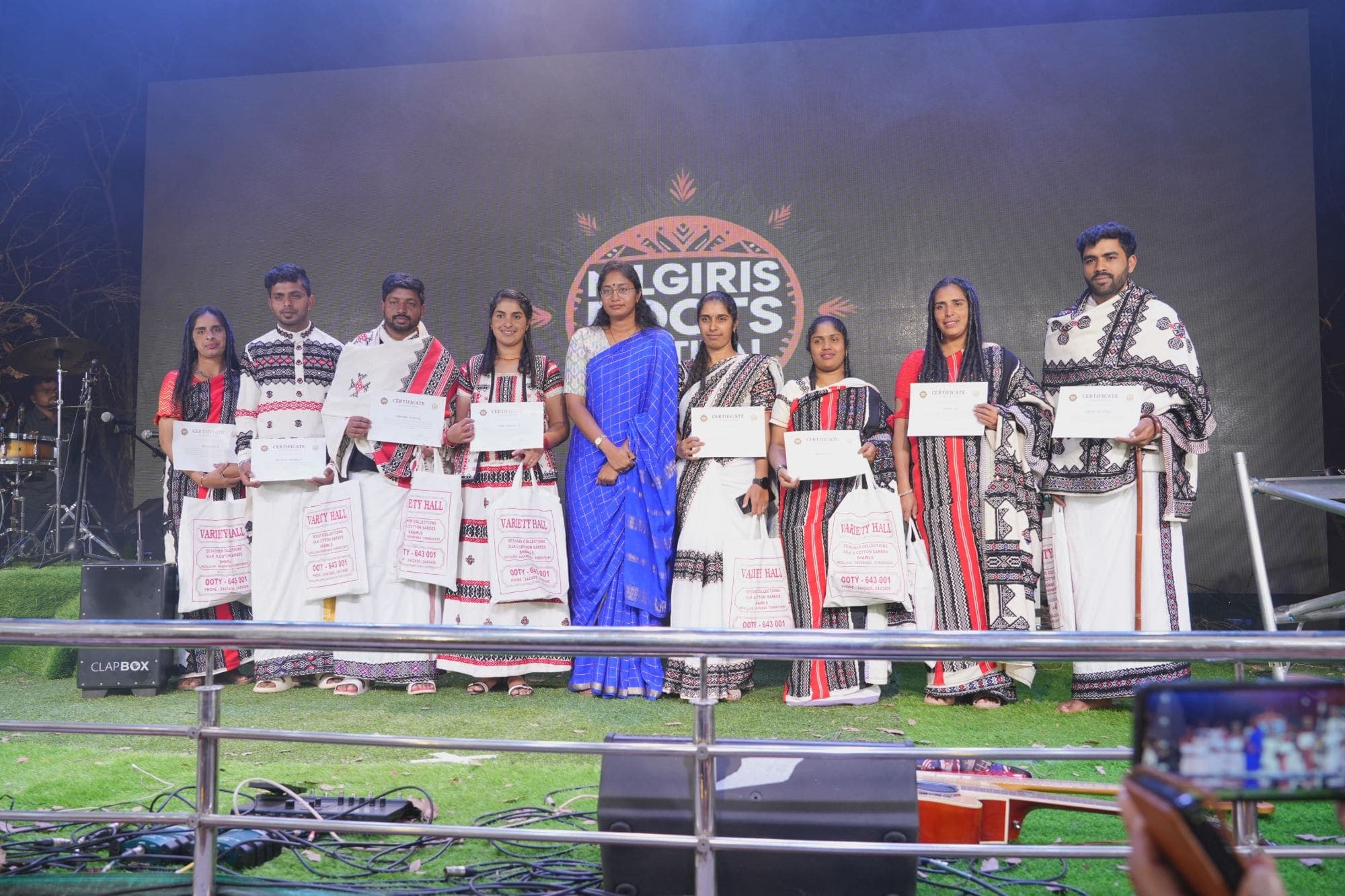 Participants in traditional dress holding their certificates on stage